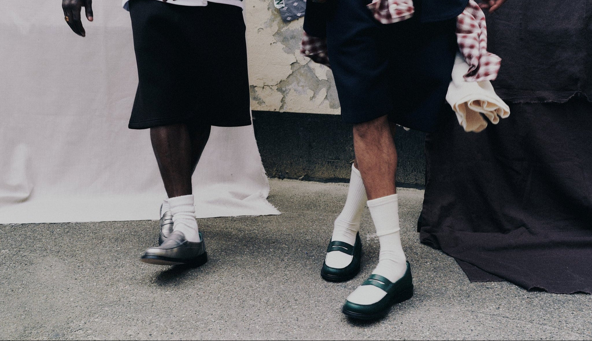 Two pairs of legs wearing black shoes and white socks against a neutral background